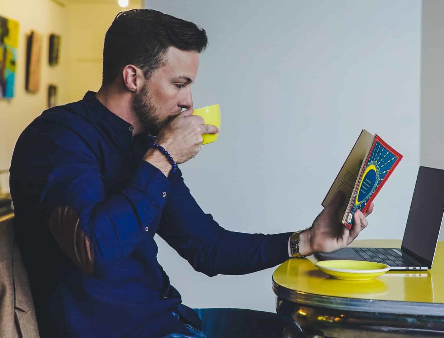 person reading book while drinking beverage